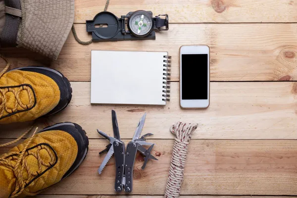 Notfallplanungsausrüstung: Kompass, Multitool, Seil, Notizbuch und Smartphone auf Holztisch